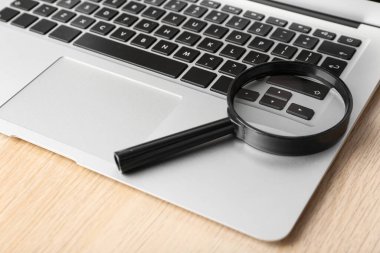 Modern laptop ve büyüteç ahşap masada, yakın plan. İnternet arama kavramı