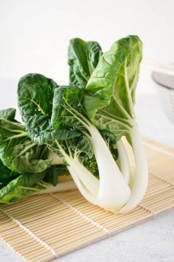 Hafif arka planda taze pak choi lahanalı bambu hasırı, yakın plan.
