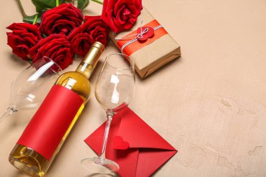 Bir şişe şarap, bardaklar, zarf, hediye ve bej arka planda güller. Sevgililer Günü kutlaması