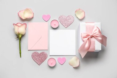 Kalpleri olan boş bir mektup, gri arka planda gül ve hediye. Sevgililer Günü kutlaması