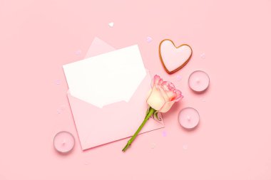 İçinde gül, kurabiye ve pembe arka planda mumlar olan boş bir mektup. Sevgililer Günü kutlaması