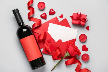 Gül, hediye, kalpler ve gri arka planda bir şişe şarap içeren boş bir mektup. Sevgililer Günü kutlaması