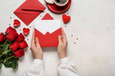 Elinde boş bir mektup, güller ve beyaz arka planda bir fincan kahve olan bir kadın. Sevgililer Günü kutlaması