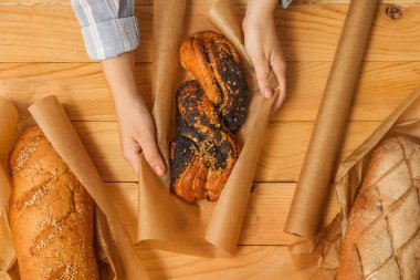 Lezzetli haşhaşlı çörekleri ambalaj kağıdıyla ahşap arka planda saran kadın.