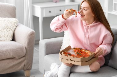 Evdeki kanepede lezzetli pizza yiyen genç bir kadın.