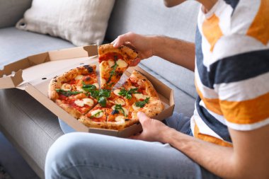 Evdeki kanepede oturmuş, bir kutu lezzetli pizzası olan genç adam.