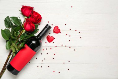 Beyaz ahşap arka planda bir şişe şarap, güller ve kalpler. Sevgililer Günü kutlaması