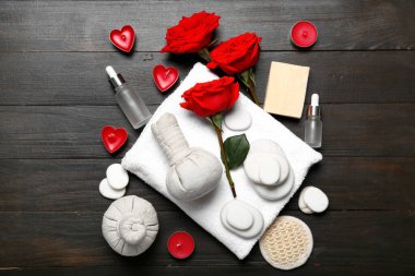 Sevgililer Günü için güzel bir spa kompozisyonu. Ahşap arka planda bitki torbaları, havlu, gül çiçekleri, sabun, taşlar ve mumlar var.