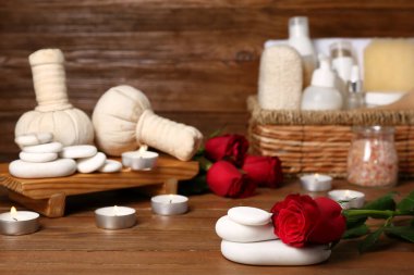 Sevgililer Günü için güzel bir spa kompozisyonu. İçinde taşlar, mumlar, gül çiçekleri ve ahşap arka planda bitki torbaları var.