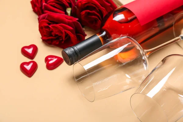 Bottle of wine, glasses, candies and roses on beige background, closeup. Valentine\'s Day celebration