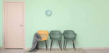 Ekoseli sandalyeler ve naneli duvarın yanında kapalı kapılı saatler. Tasarım için pankart