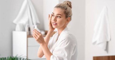 Güzel genç bir kadın banyoda cildine kozmetik yağı sürüyor.