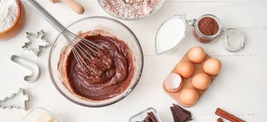 Taze çikolata hamuru ve beyaz ahşap arka planda tatlı malzemeleriyle dolu bir kase.