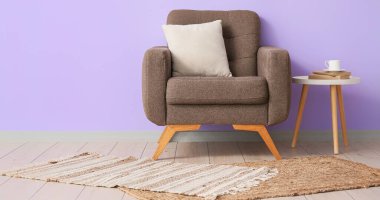 Rahat koltuk, halı, kahve fincanı ve odada leylak duvarının yanında kitaplar.