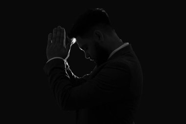 Karanlık arka planda dua eden genç adamın silueti.