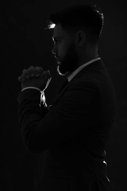 Karanlık arka planda dua eden genç adamın silueti.