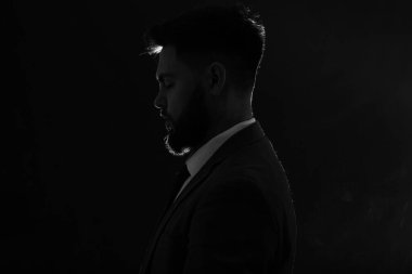 Siyah arka planda takım elbiseli genç adam silueti, yakın plan.