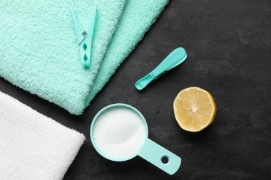 Çamaşır deterjanı, limon ve siyah arka planda havlular.