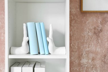 Pembe duvarın yanında şık kitap destekli raf ünitesi.