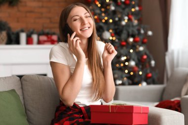 Yılbaşı hediyesiyle evde cep telefonuyla konuşan genç bir kadın.