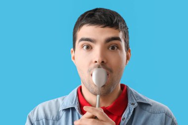 Mavi arka planda gümüş kaşıklı genç adam, yakın plan.