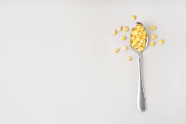 Gri arkaplanda konserve mısır taneleri olan kaşık