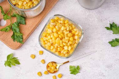 Mısır taneli kase, tahta, kaşık ve maydanozlu beyaz masa.