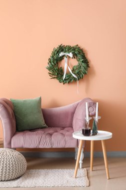 Oturma odasının içinde Noel çelengi, koltuk ve masa var.