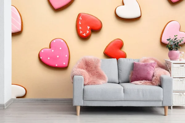 Grey sofa near beige wall with printed heart shaped cookies in room