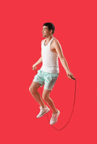 Sporty young man jumping with rope on red background