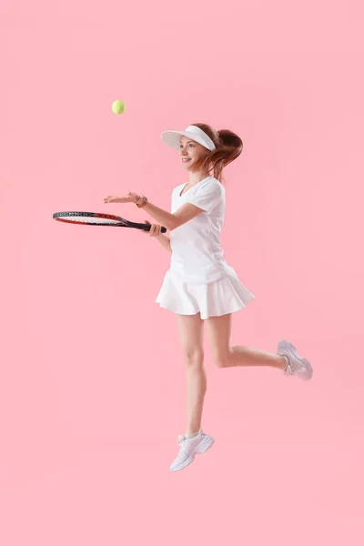 Young female tennis player with racket and ball jumping on pink background