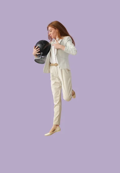 Female Geography teacher with globe jumping near lilac wall
