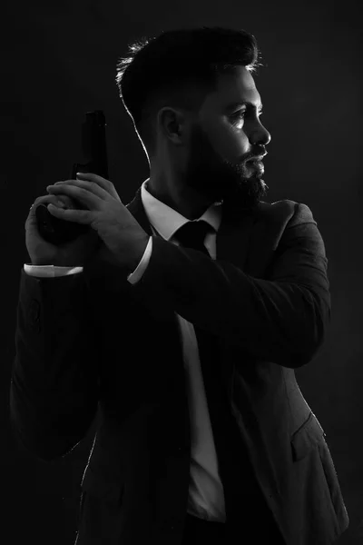 Silhouette of young man in suit with gun on dark background