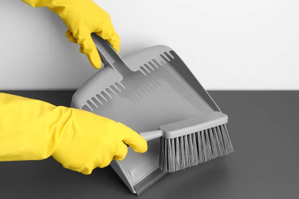 Female hands in rubber gloves with dustpan and brush on floor, closeup