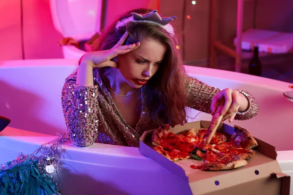 Drunk young woman with pizza in bathtub after party