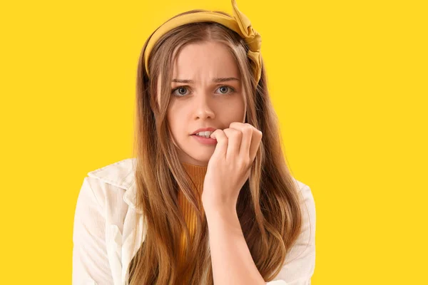 Young woman biting nails on yellow background, closeup
