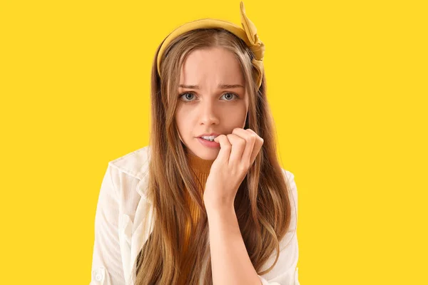 Young woman biting nails on yellow background, closeup