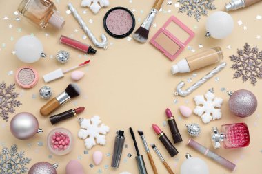 Farklı kozmetik ürünleri, makyaj aksesuarları ve renk arkaplanındaki Noel süslerinden yapılmış çerçeve