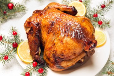 Lezzetli tavuk, limon dilimleri, böğürtlen ve beyaz arka planda Noel dallarıyla dolu bir tabak.