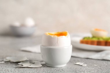 Haşlanmış yumurta ve kabuklu tutucu gri masada.