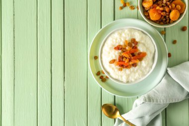 Lezzetli sütlaç, kuru üzüm, kurutulmuş kayısı ve yeşil ahşap masada kaşık.