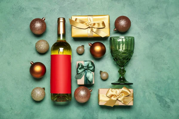 Bottle of wine with glass, Christmas balls and gifts on green background
