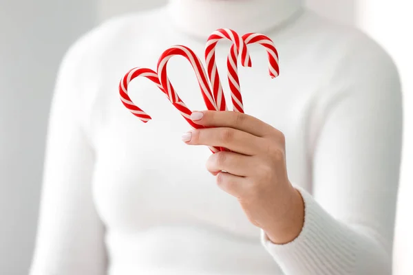 Woman holding sweet candy canes on light background, closeup