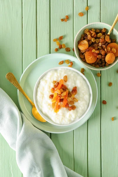 Lezzetli sütlaç, kuru üzüm, kurutulmuş kayısı ve yeşil ahşap masada kaşık.