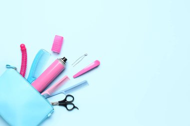 Mavi arka planda saç spreyi, tarak, ataç ve makas dolu çanta.