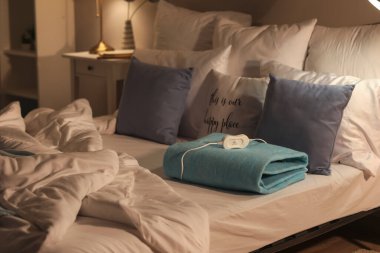 Geceleri yatak odasında katlanmış elektrikli ısıtma yastığı olan bir yatak.