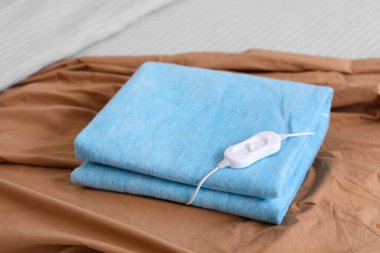 Katlanmış elektrikli ısıtma yastığı ve kontrol cihazı odada, yakın plan.