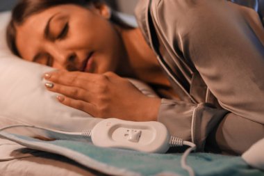 Geceleri yatak odasındaki elektrikli ısıtma yastığında uyuyan genç bir kadın.