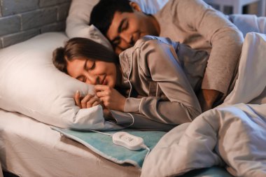 Genç çift geceleri yatak odasındaki elektrikli ısıtma yastığında uyuyor.