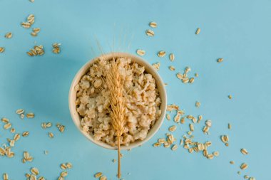 Lezzetli yulaf ezmeli kase, buğday kulaklı ve mavi arka planda dağınık taneli.